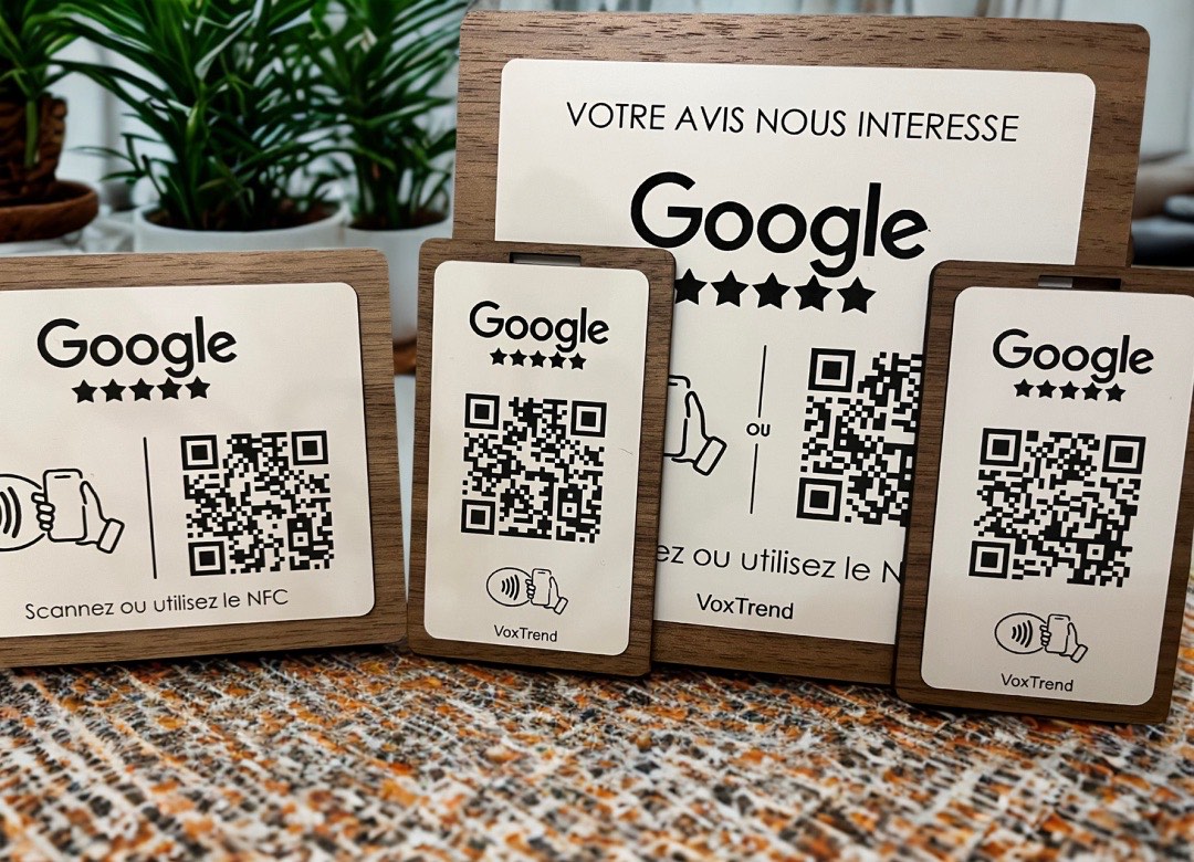 Le kit VoxTrend posé sur un comptoir : une plaquette de porte, un chevalet et deux badges, chacun avec le logo Google, cinq étoiles et un QR code, montés dans un cadre bois.